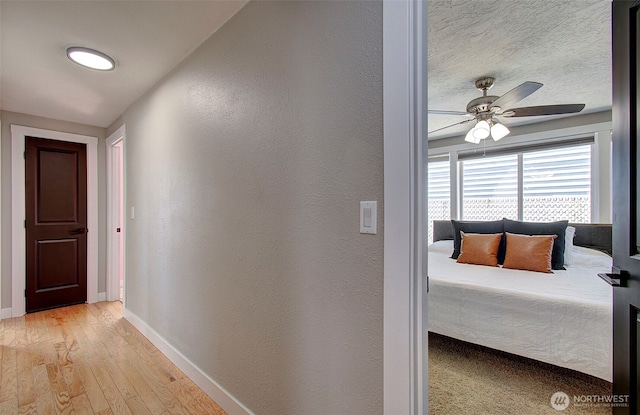 hall featuring baseboards, light wood-style flooring, and a textured wall