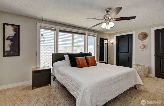 bedroom featuring light colored carpet, baseboards, a textured ceiling, and a ceiling fan