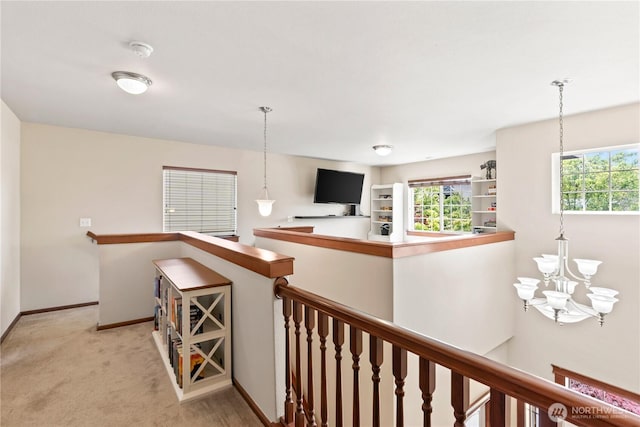 hall with an upstairs landing, a chandelier, baseboards, and light colored carpet