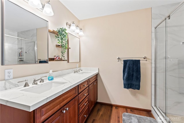 full bath featuring wood finished floors, a shower stall, double vanity, and baseboards