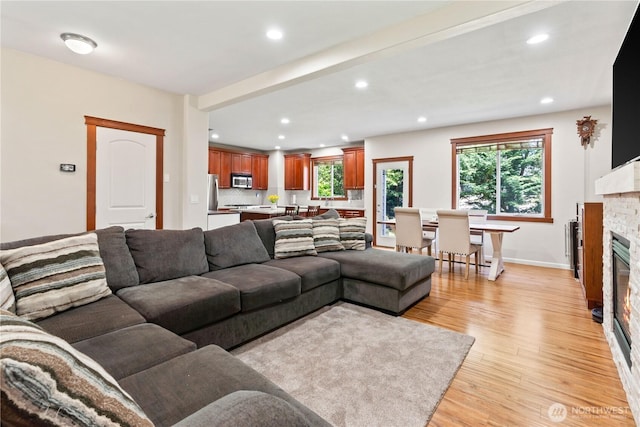 living room with light wood finished floors, recessed lighting, a glass covered fireplace, plenty of natural light, and baseboards