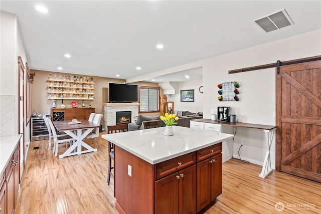kitchen with light wood-style floors, a barn door, a breakfast bar, a stone fireplace, and recessed lighting