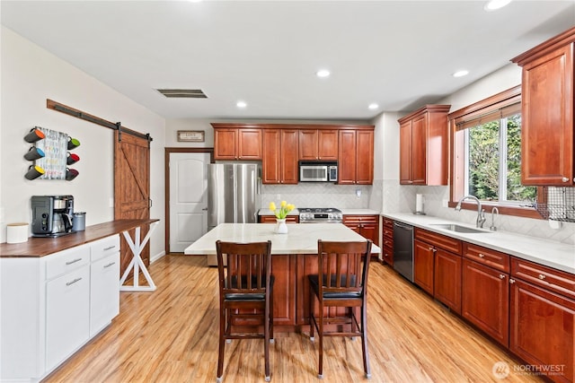kitchen with a sink, appliances with stainless steel finishes, a barn door, light wood-type flooring, and a breakfast bar area
