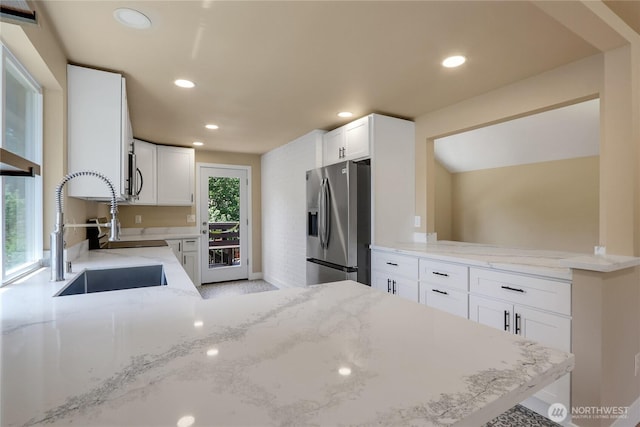 kitchen with appliances with stainless steel finishes, a sink, a peninsula, recessed lighting, and light stone counters