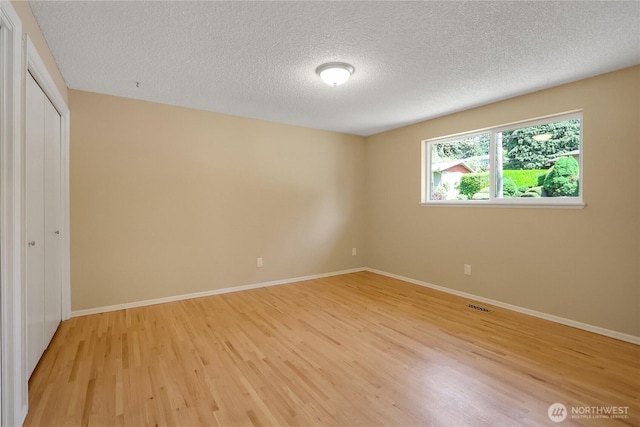 unfurnished bedroom featuring light wood-type flooring, a textured ceiling, baseboards, and a closet