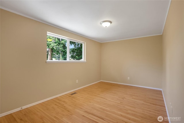 empty room with light wood-type flooring, baseboards, and crown molding