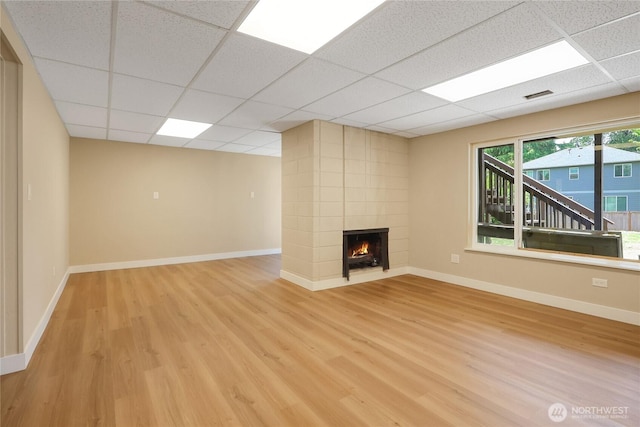 unfurnished living room with light wood-style floors, a paneled ceiling, a large fireplace, and baseboards