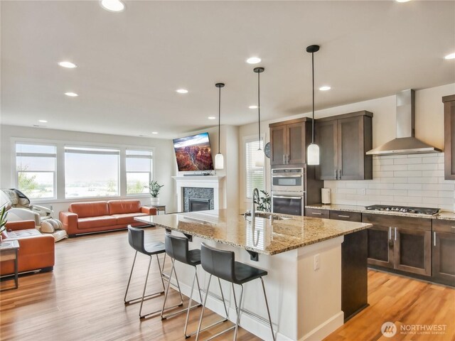 2668 83rd Avenue Ct E, Edgewood, WA 98371 - kitchen with wall chimney exhaust hood, stainless steel appliances, open floor plan, a sink, and a kitchen breakfast bar
