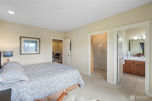 bedroom featuring light colored carpet, a walk in closet, baseboards, ensuite bath, and a closet