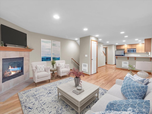 living room with a tiled fireplace, light wood-style floors, recessed lighting, and baseboards