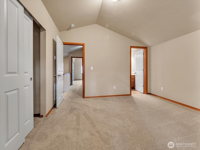 unfurnished bedroom featuring vaulted ceiling, light colored carpet, baseboards, and ensuite bathroom