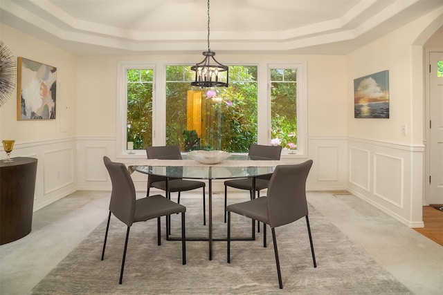 dining space featuring a decorative wall, a raised ceiling, healthy amount of natural light, a chandelier, and a wainscoted wall