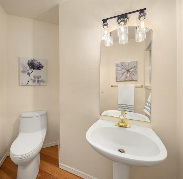 bathroom featuring wood finished floors, toilet, baseboards, and a sink