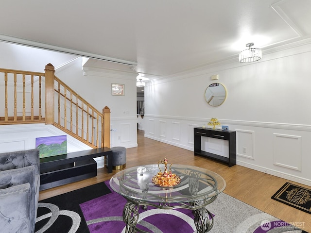 living area featuring wood finished floors, ornamental molding, stairway, a decorative wall, and wainscoting