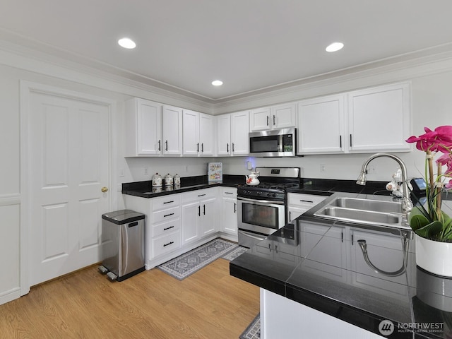 kitchen with appliances with stainless steel finishes, a sink, light wood-style floors, white cabinetry, and crown molding