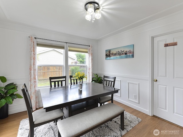 dining space featuring ornamental molding, light wood-style floors, wainscoting, and a decorative wall