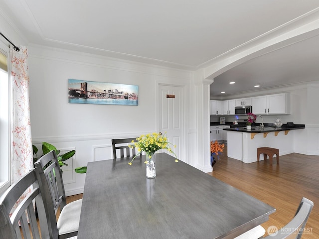 dining area with wood finished floors, arched walkways, recessed lighting, and ornamental molding