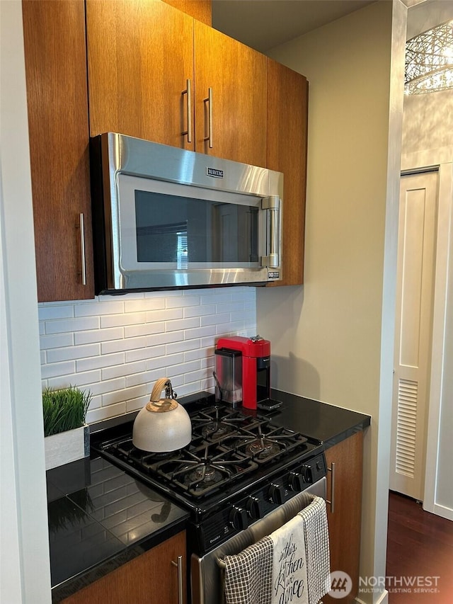 2721 1st Ave Unit 103, Seattle, WA 98121 - kitchen with stainless steel microwave, range with gas cooktop, tasteful backsplash, dark countertops, and brown cabinetry