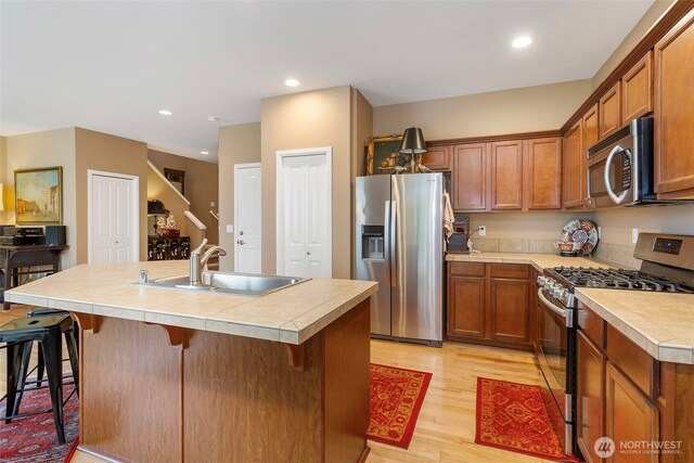 kitchen featuring stainless steel appliances, a sink, light wood-style flooring, a kitchen breakfast bar, and brown cabinetry