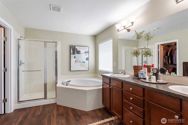 bathroom featuring a stall shower, a garden tub, wood finished floors, double vanity, and a walk in closet