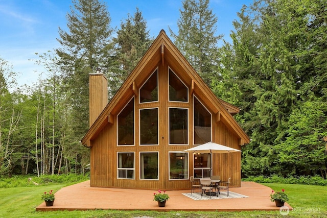 back of property with a chimney, a deck, a yard, and a view of trees