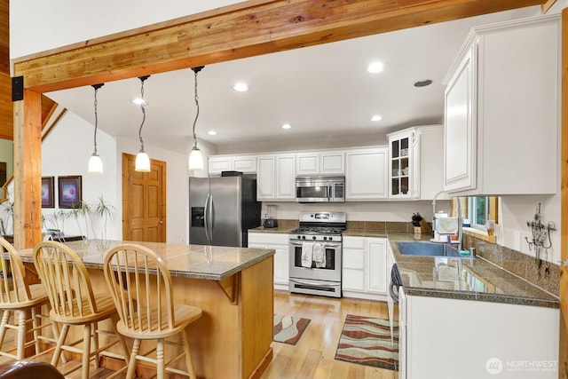 kitchen with stainless steel appliances, a sink, tile counters, a breakfast bar, and light wood-type flooring
