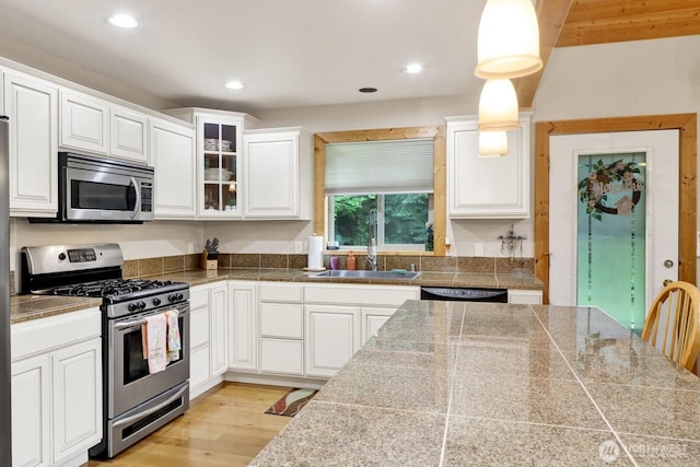 kitchen with appliances with stainless steel finishes, tile counters, a sink, glass insert cabinets, and white cabinets