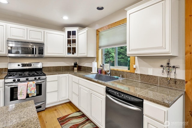 kitchen with appliances with stainless steel finishes, tile counters, a sink, light wood finished floors, and white cabinetry