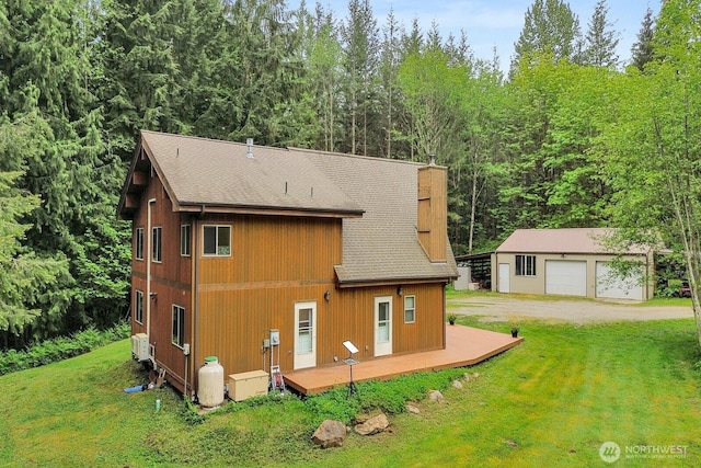 back of property featuring a yard, a shingled roof, an outdoor structure, a detached garage, and a deck