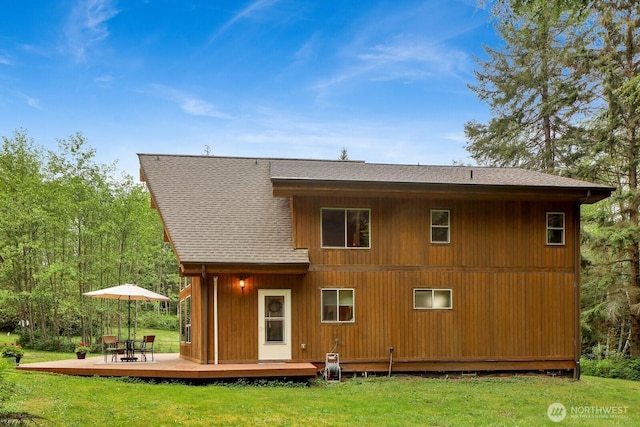 rear view of house with a deck, a lawn, and roof with shingles