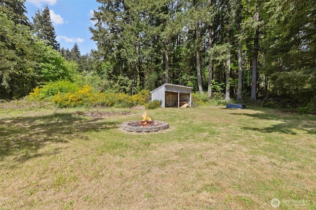 view of green lawn featuring a fire pit, a detached carport, and an outbuilding