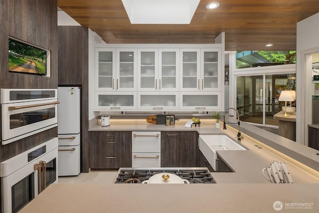 kitchen with white appliances, a sink, dark brown cabinets, white cabinetry, and wooden ceiling