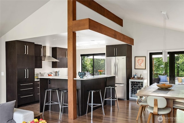 kitchen with wall chimney range hood, wine cooler, stainless steel refrigerator, light countertops, and modern cabinets