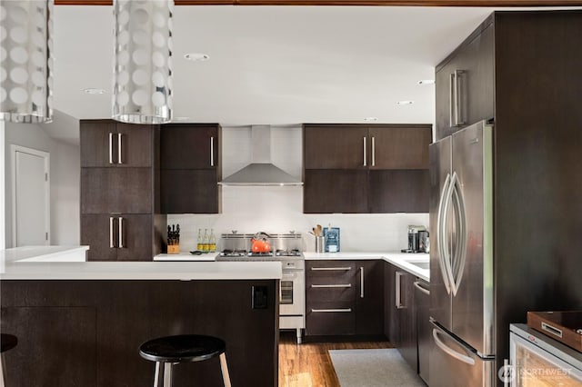 kitchen with wall chimney exhaust hood, stainless steel appliances, a breakfast bar area, wood finished floors, and light countertops