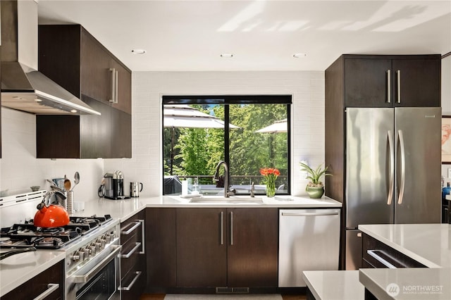 kitchen featuring stainless steel appliances, a sink, wall chimney exhaust hood, light countertops, and backsplash