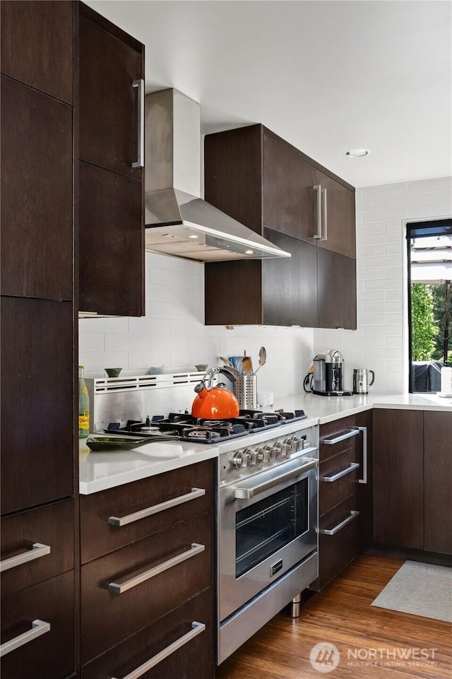 kitchen with wall chimney exhaust hood, stainless steel range with gas stovetop, dark wood finished floors, and tasteful backsplash