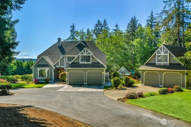 english style home with a garage, concrete driveway, a front yard, and a chimney