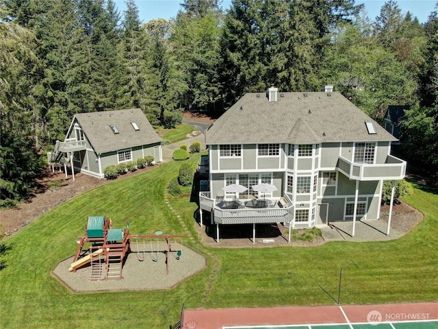 back of property with a playground, a lawn, stucco siding, roof with shingles, and a balcony