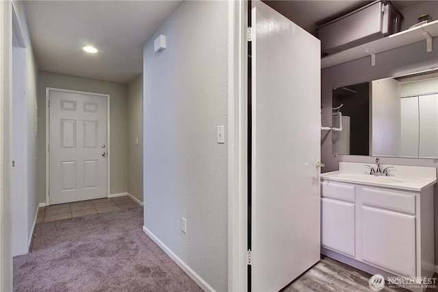 hallway featuring a sink, baseboards, and light colored carpet