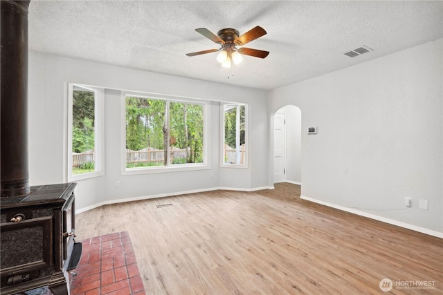 10320 16th St E, Edgewood, WA 98372 - unfurnished living room with a wood stove, ceiling fan, arched walkways, wood finished floors, and a textured ceiling