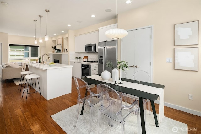 kitchen with stainless steel appliances, an island with sink, white cabinets, a kitchen bar, and backsplash
