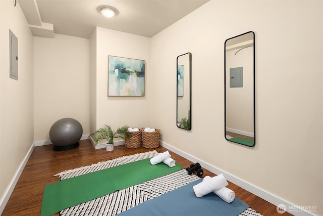 exercise area with electric panel, wood finished floors, and baseboards
