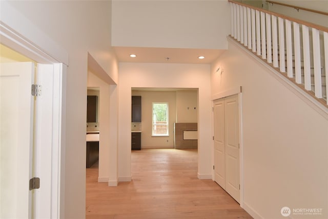 hallway with light wood-type flooring, a high ceiling, recessed lighting, and baseboards