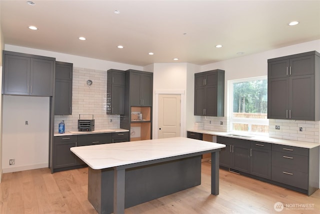 kitchen featuring decorative backsplash, light stone countertops, light wood-style flooring, a center island, and recessed lighting