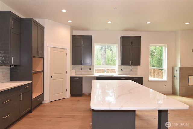 kitchen featuring light wood-style flooring, backsplash, recessed lighting, light stone counters, and a kitchen island