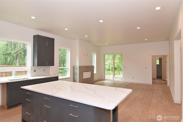 kitchen with light wood finished floors, recessed lighting, decorative backsplash, a center island, and light stone counters