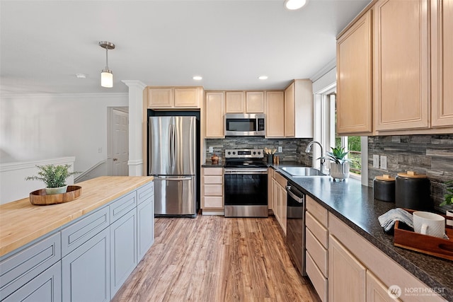 kitchen featuring appliances with stainless steel finishes, a sink, decorative backsplash, light wood finished floors, and wood counters