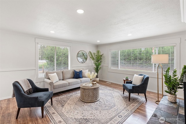 living room with ornamental molding, a textured ceiling, light wood-style flooring, baseboards, and recessed lighting