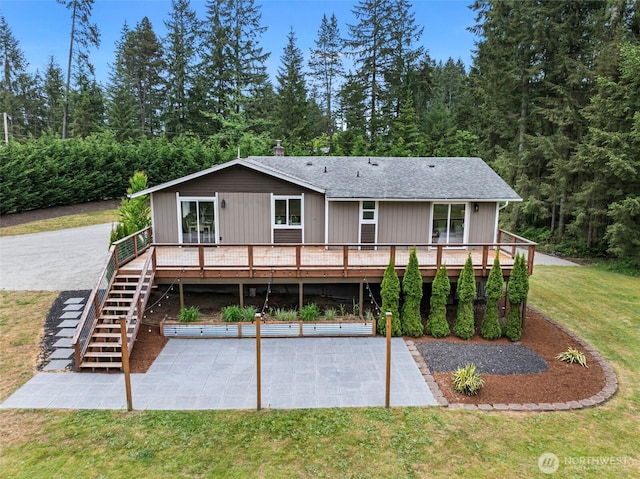 back of property with a yard, a deck, a patio area, stairway, and roof with shingles