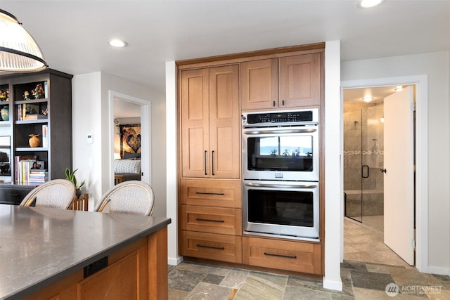 kitchen featuring stainless steel double oven, recessed lighting, light stone finish flooring, and baseboards